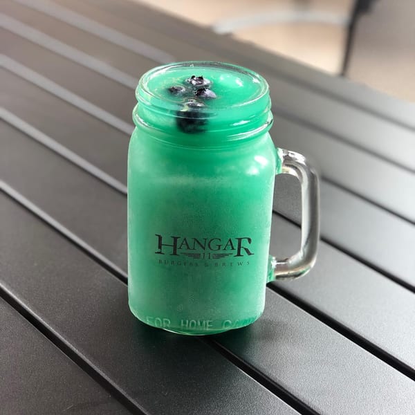 A Hangar 11 Burgers & Brews mason jar mug filled with a green frozen drink and blueberries.