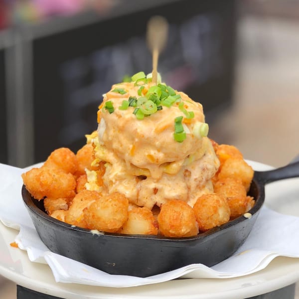 Hangar 11 Burgers' tater tots in a cast iron skillet, topped with melted cheese and green onions.