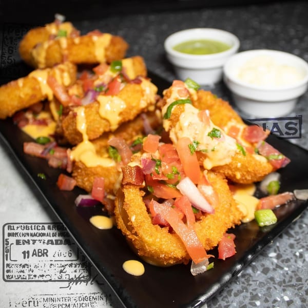 Crispy onion rings topped with cheese sauce, diced tomatoes, and red onions, with dipping sauces.