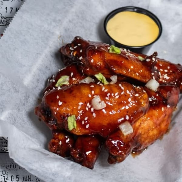 Hangar 11 Burgers' sticky BBQ wings, topped with sesame seeds and green onions, with a side of dipping sauce.